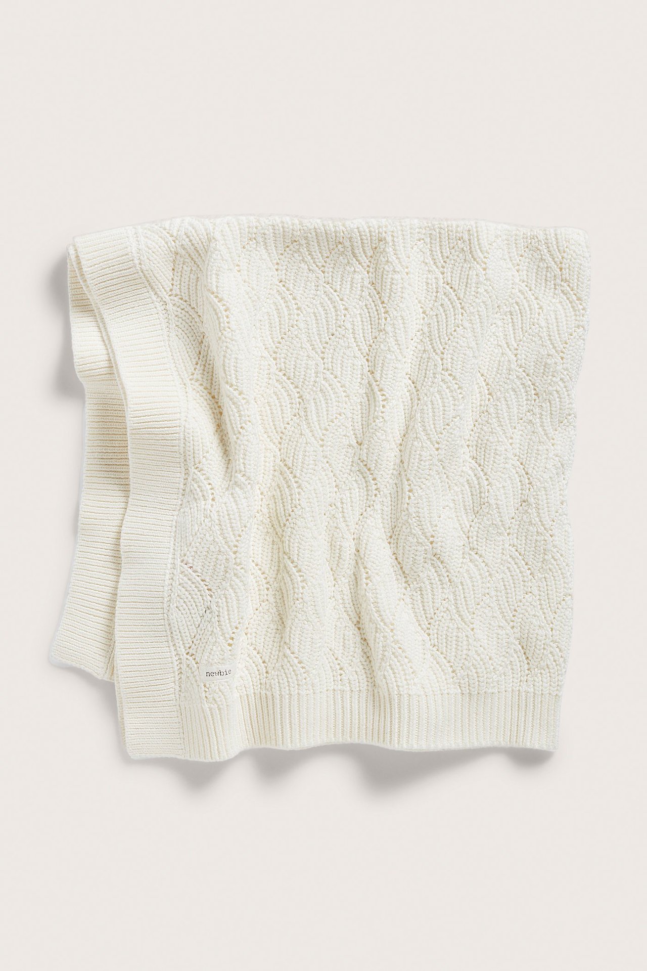 Uppifrån vy av en offwhite stickad babyfilt i bomull med jacquardmönster och ribbade kanter.