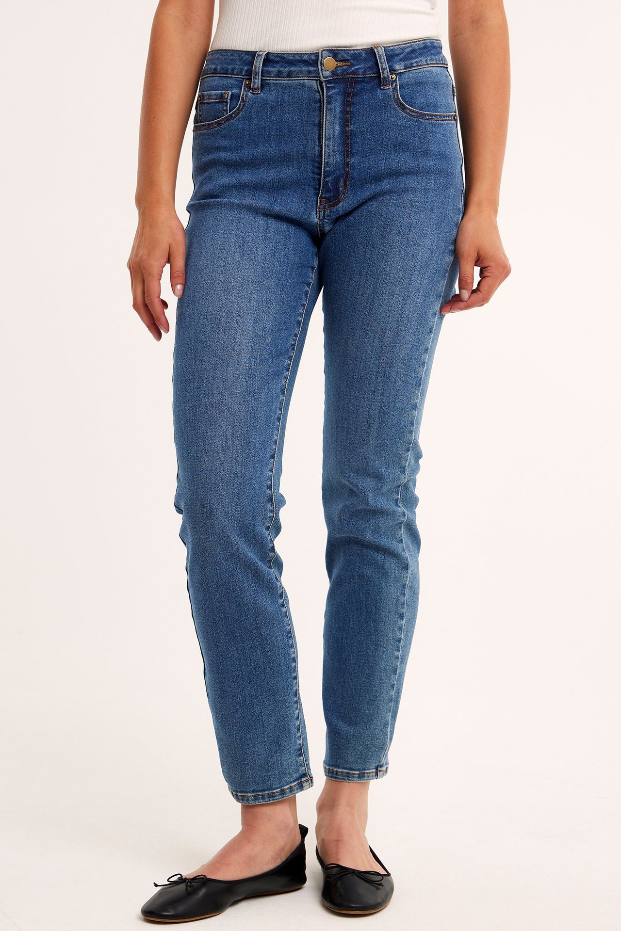 Framifrån, kvinna i blå raka högmidjade denimjeans, vit ribbad topp och svarta ballerinaskor.