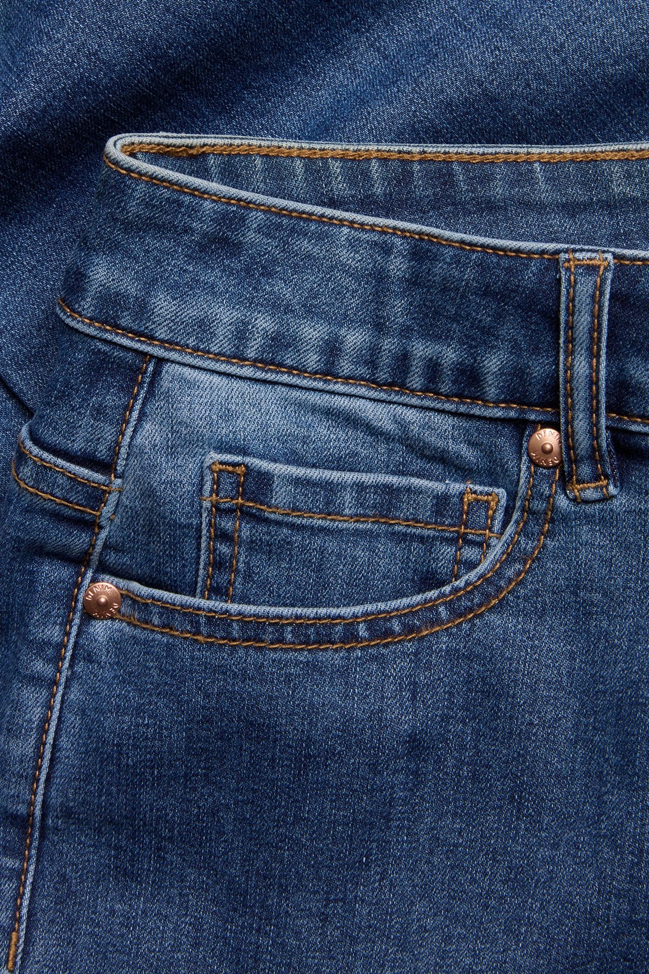 Zbliżenie na niebieskie dżinsy z wysokim stanem, z przednią kieszenią, brązowymi szwami i metalowym nitem.