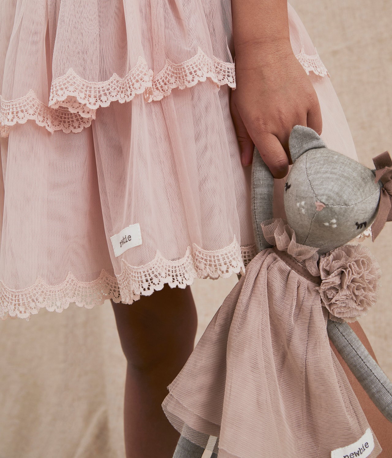 Närbild: Barn håller en beige melerad bomullskanin i rosa tyllklänning, bärande en rosa volangklänning.