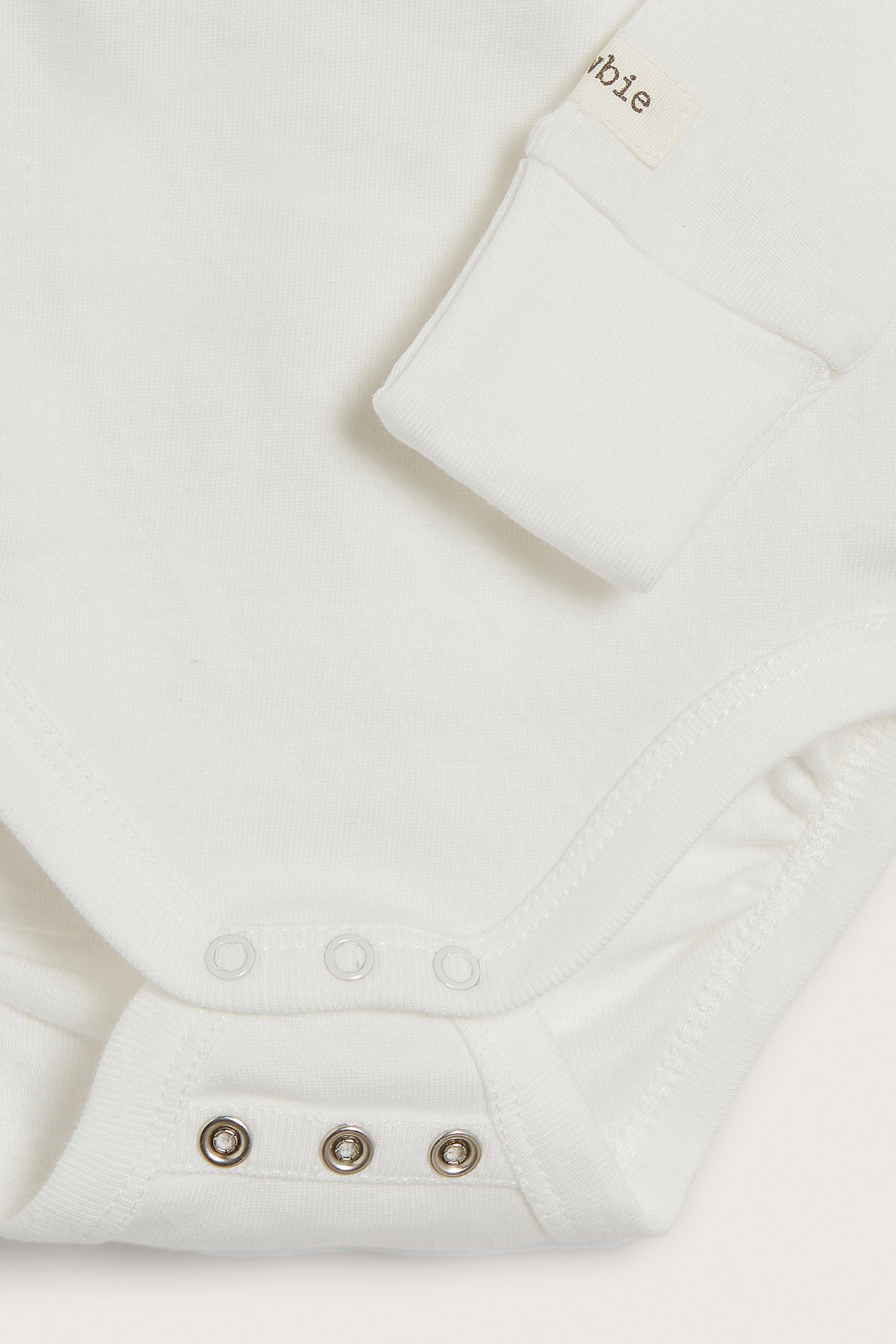 Nærbilde av en offwhite langermet omslagsbody for baby med trykknapper i skrittet.