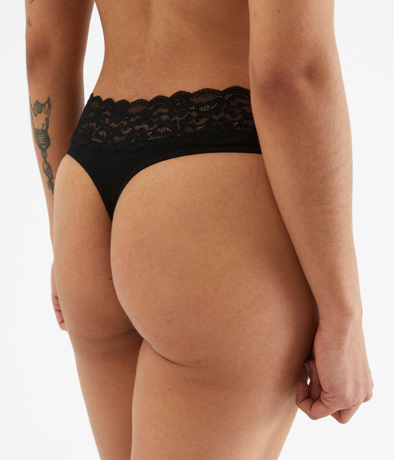 Lähikuva takaa naisesta, joka käyttää mustia puuvillaisia stringejä leveällä pitsireunuksella vyötäröllä.