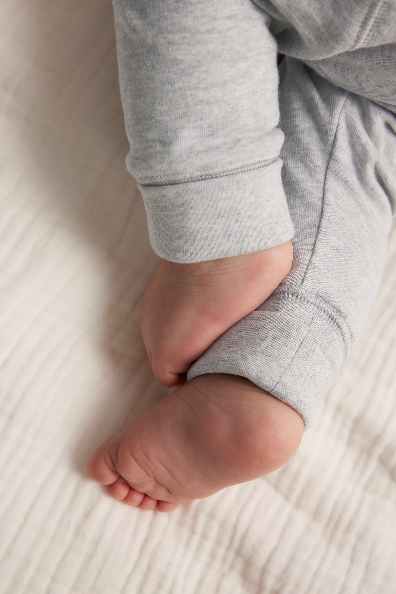 Lähikuva vauvasta harmaamelange-puuvillaleggingsseissä taitetuilla resoreilla, paljaat jalat näkyvissä.