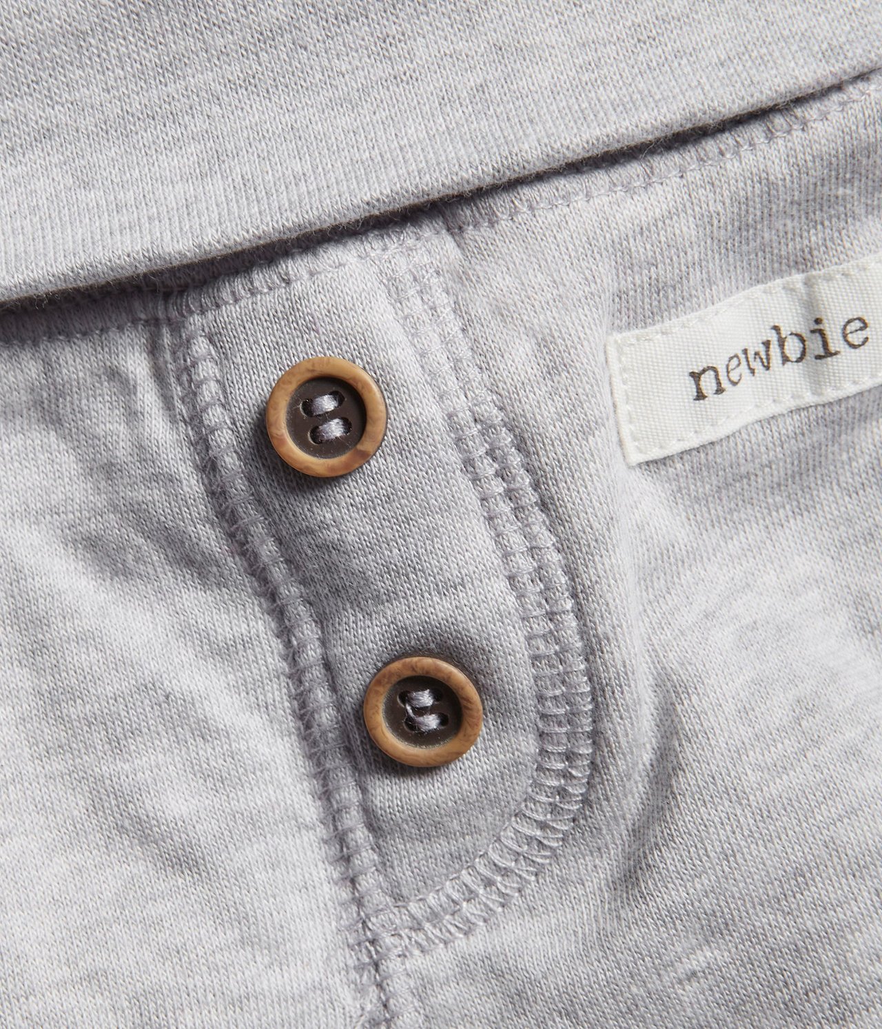 Zbliżenie na szare melanżowe bawełniane legginsy niemowlęce z dwoma ozdobnymi brązowymi guzikami i białą metką.
