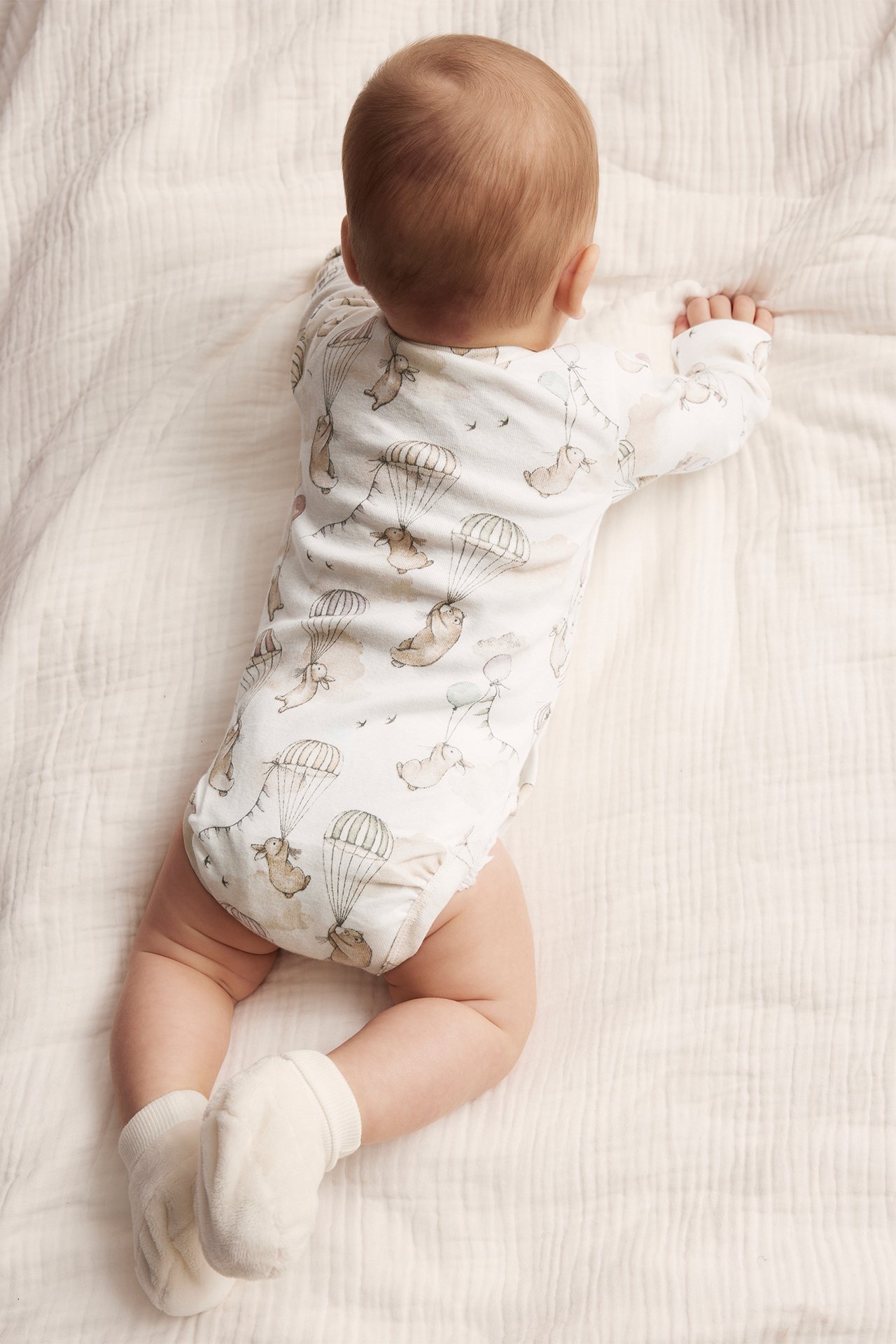 Vauvan selkäpuoli offwhite-kuviollisessa pitkähihaisessa bodyassa, jossa on pupukuvio ja offwhite-sukat.