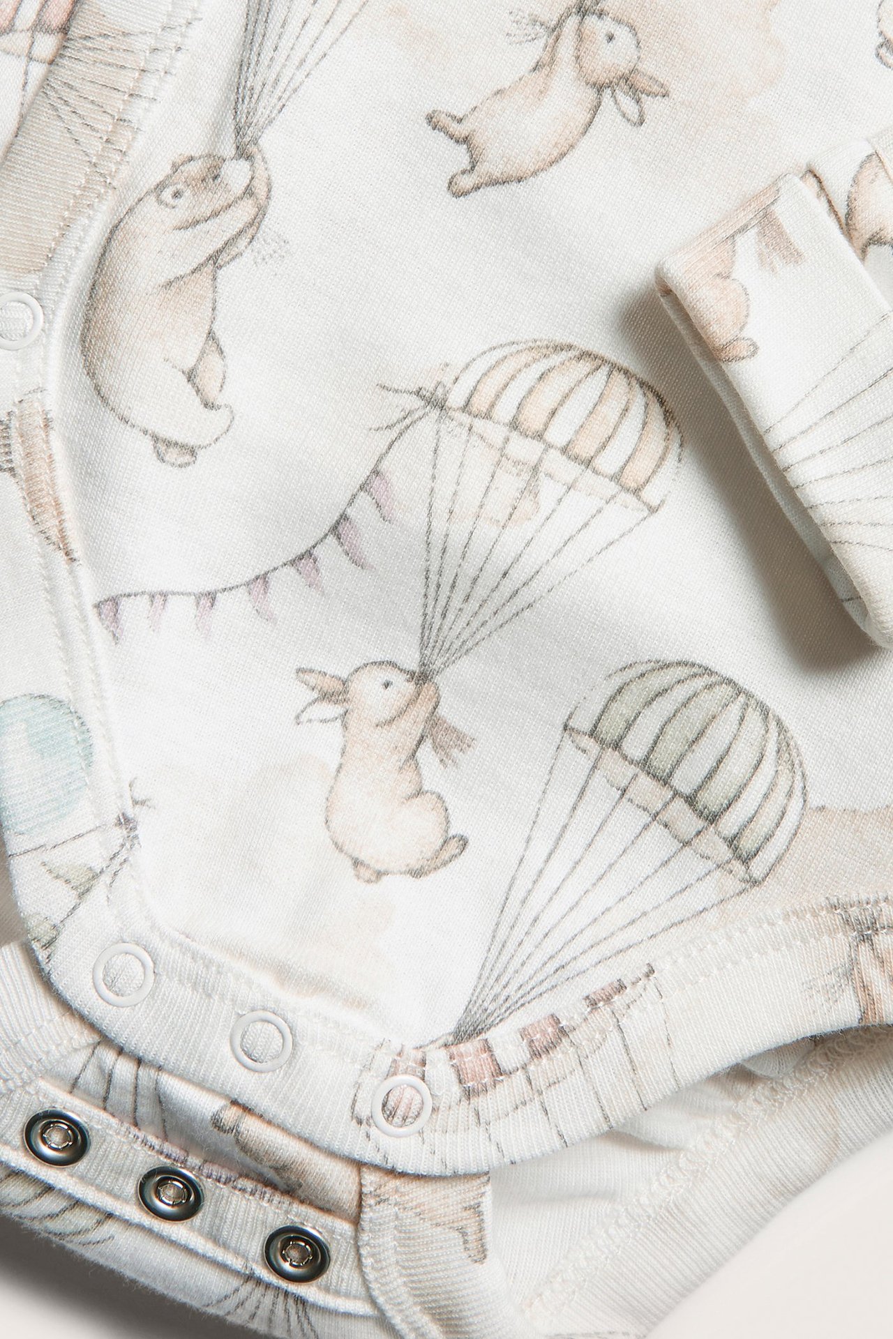 Zbliżenie na ecru body kopertowe dla niemowląt z nadrukiem królików, niedźwiedzi i balonów, z zatrzaskami.