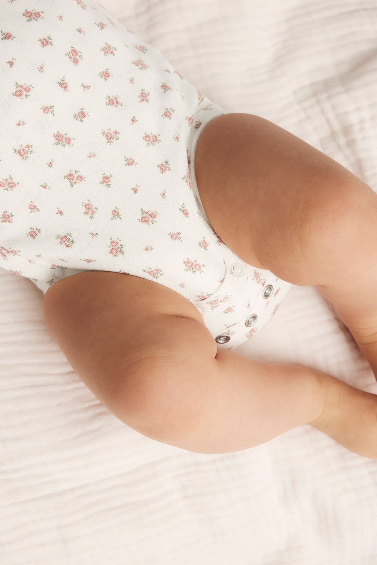 Närbild på en baby i en offwhite bomullsbody med rosa blommönster och tryckknappar.