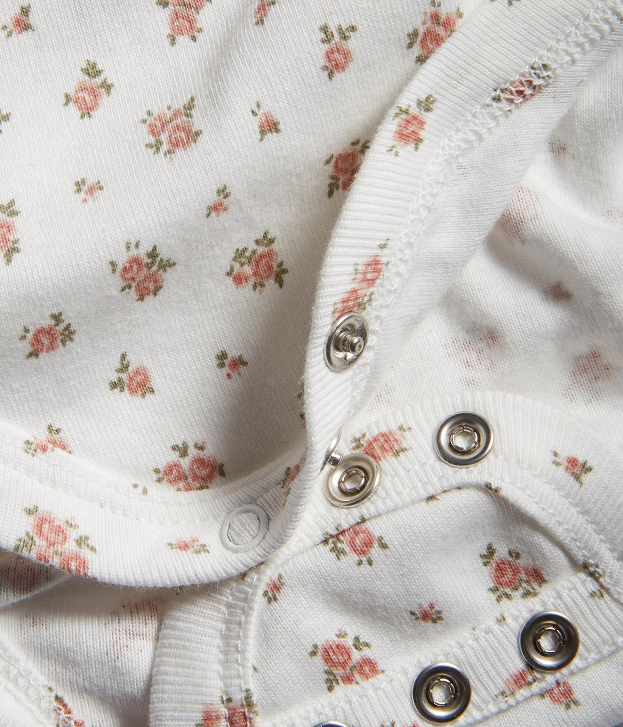 Zbliżenie na ecru bawełniane body niemowlęce z różowym kwiatowym wzorem i zatrzaskami.