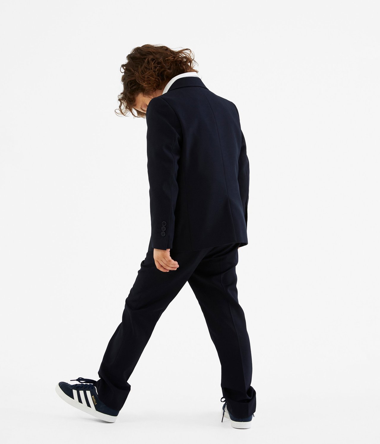 Lapsen takaa näkymä tummansinisessä bleiserissä, valkoisessa paidassa, tummansinisissä housuissa ja lenkkareissa.