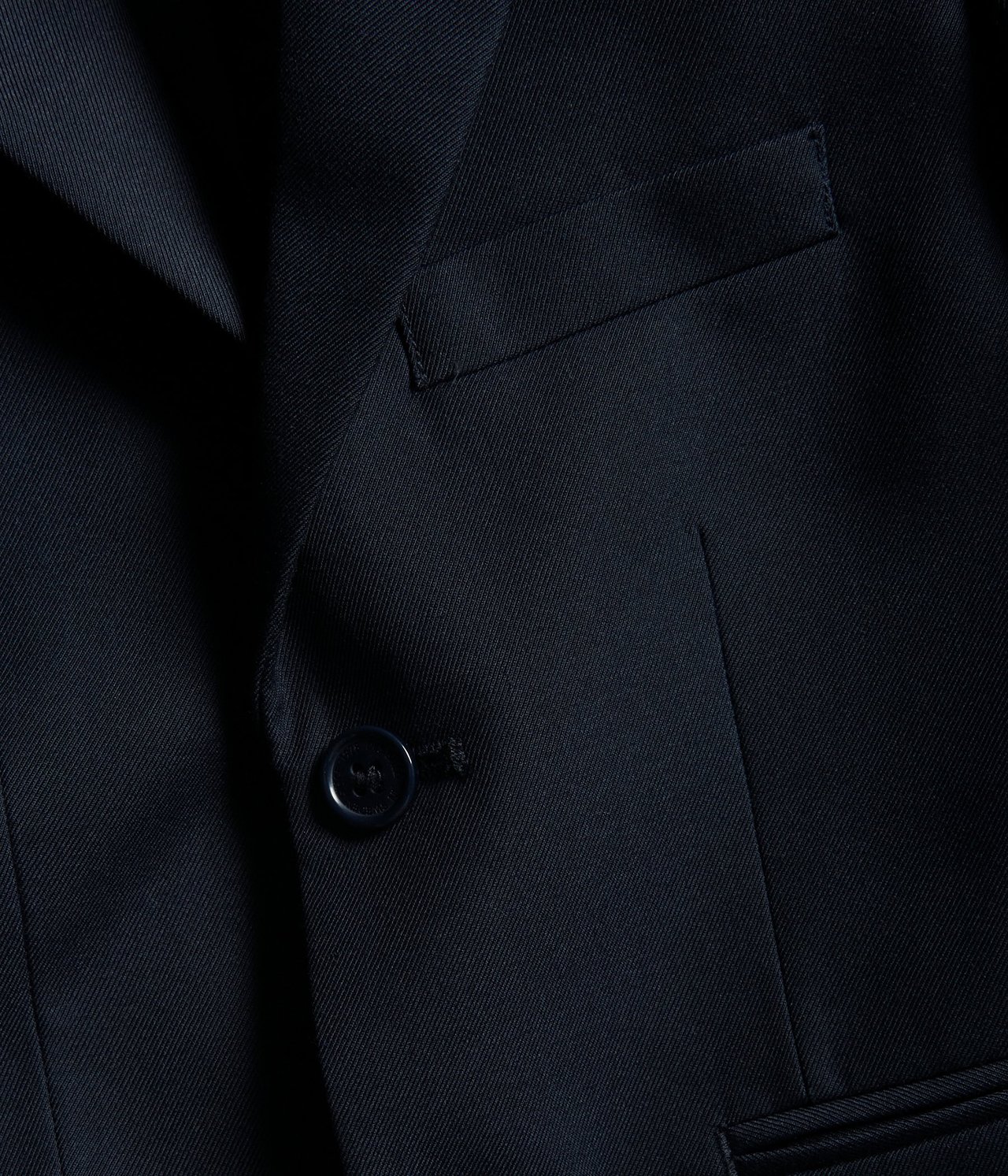 Zbliżenie na granatową marynarkę z jednym guzikiem i kieszenią z wypustką.