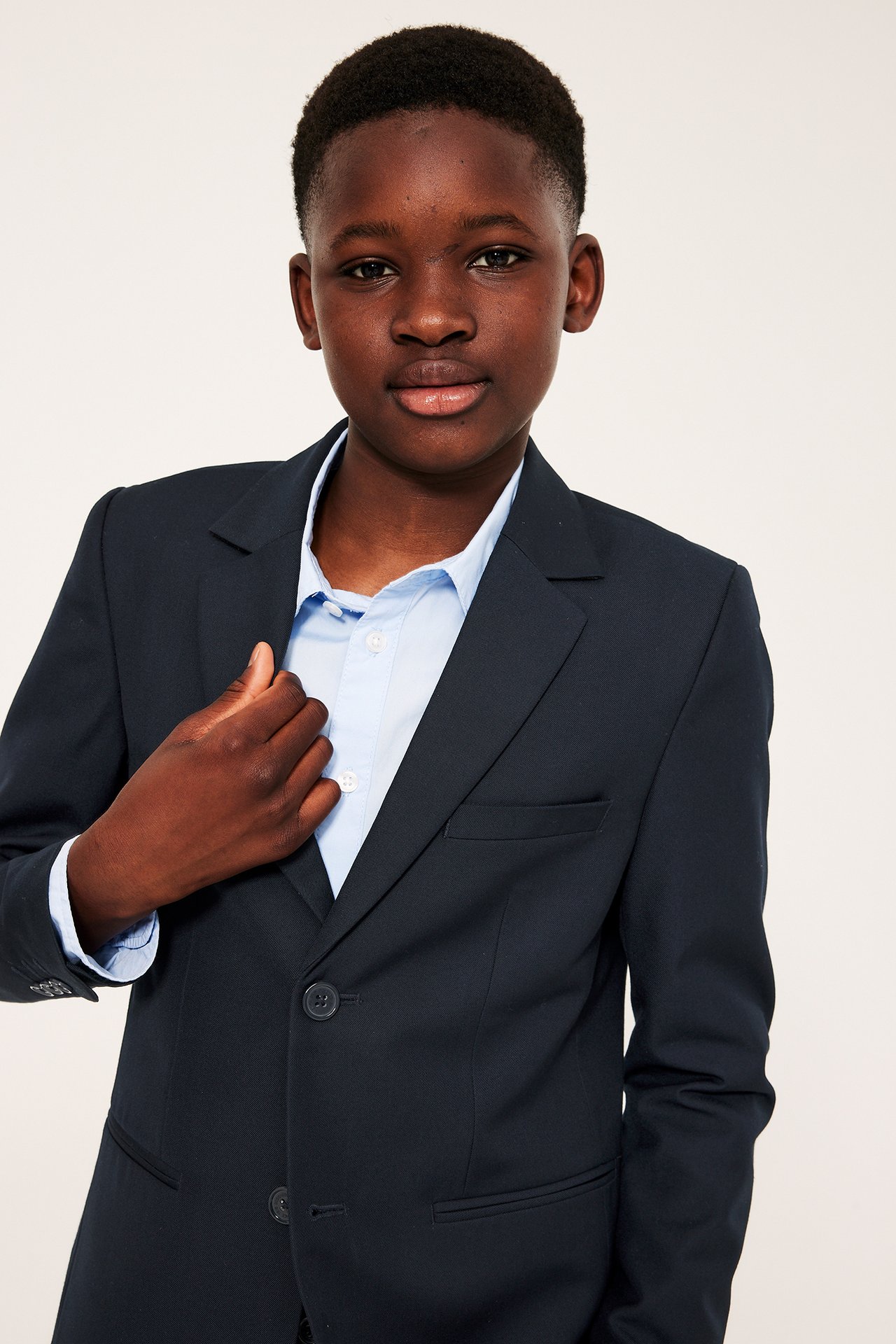 Framifrån, ett barn i mörkblå kavaj med tre passpoalfickor över en ljusblå skjorta.