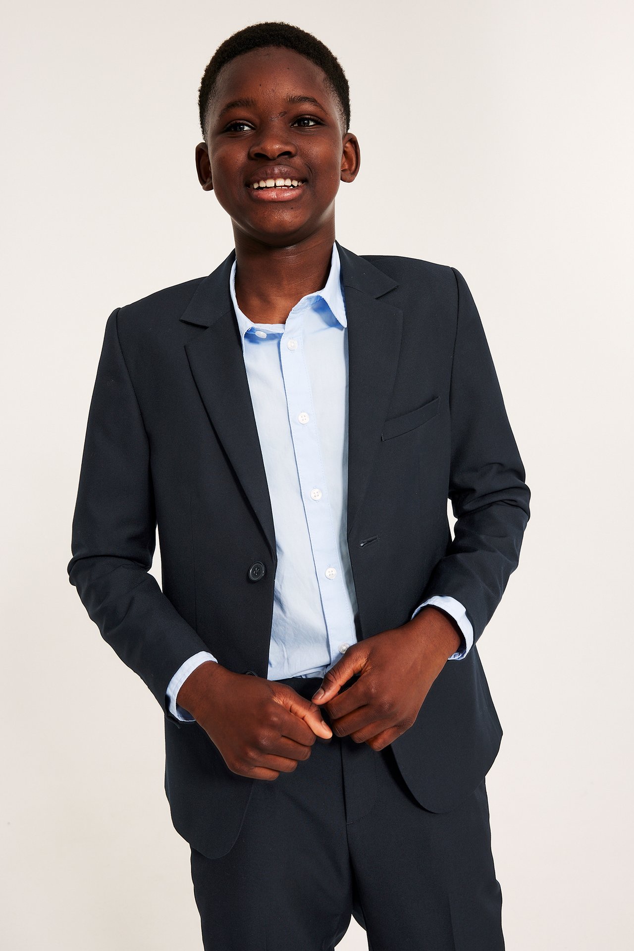 Widok z przodu: dziecko w granatowej marynarce z guzikiem, na jasnoniebieskiej koszuli i granatowych spodniach.