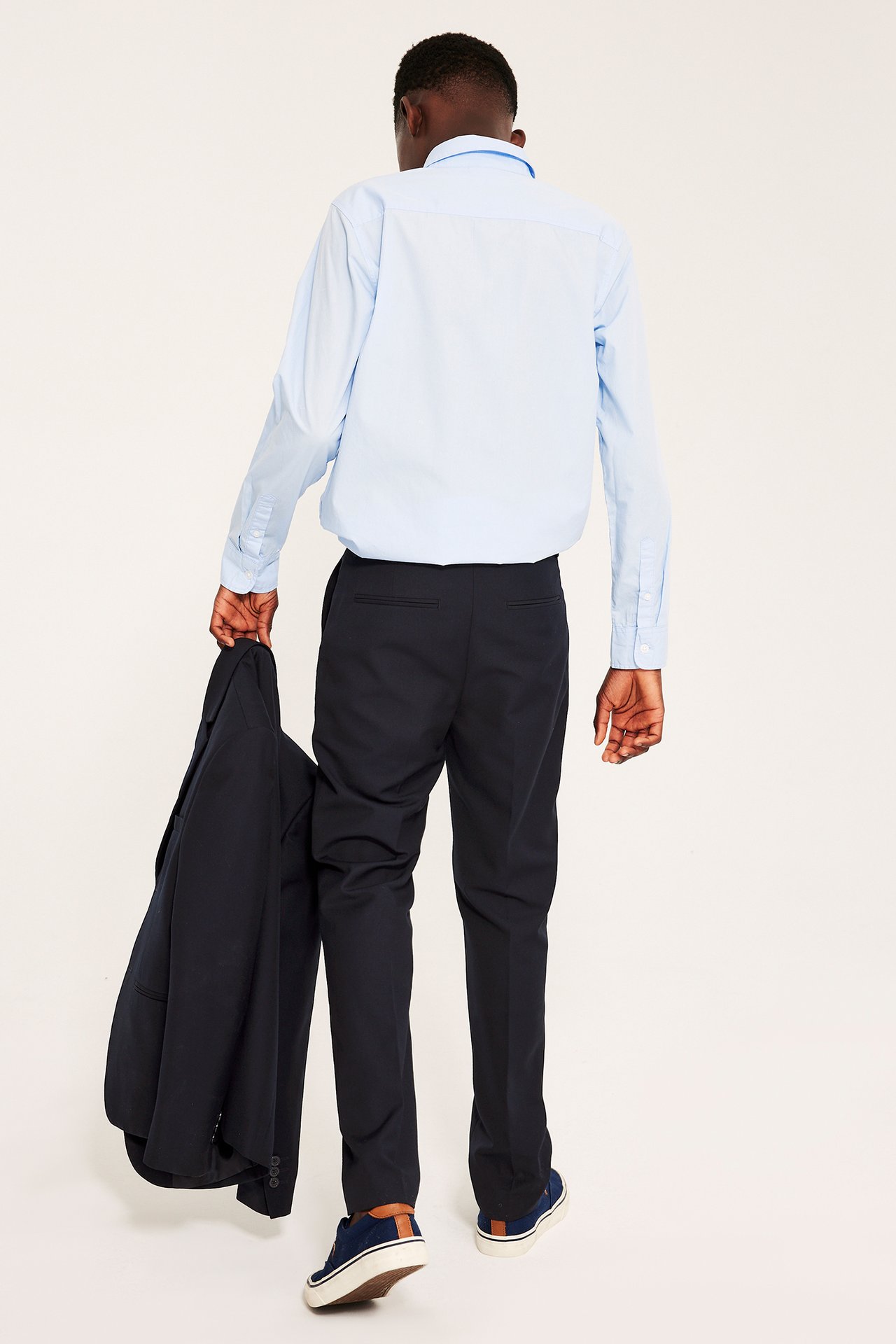 Lapsi takaa: tummansiniset pukuhousut, vaaleansininen paita ja kädessä tummansininen bleiseri.