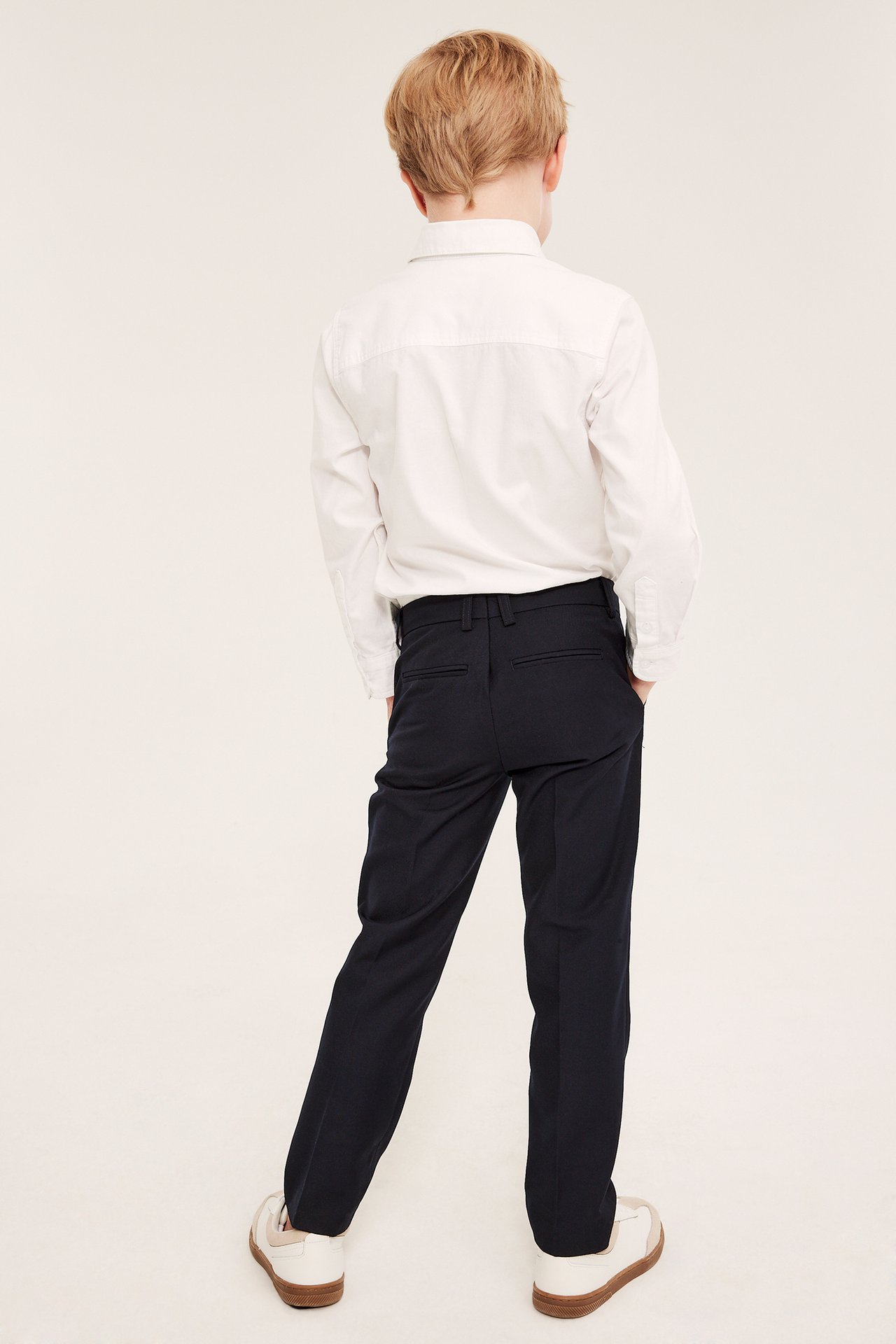 Bakfra et barn i mørkeblå ensfargede dressbukser med press og en hvit langermet skjorte.