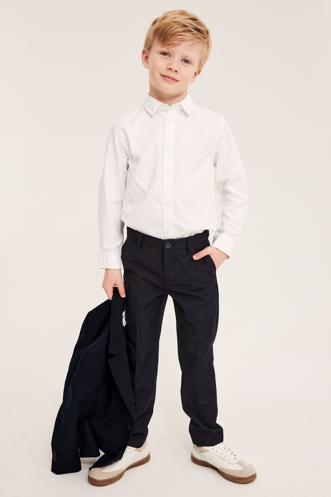 Front view: Barn i mörkblå kostymbyxor, vit skjorta, håller en mörkblå kavaj.