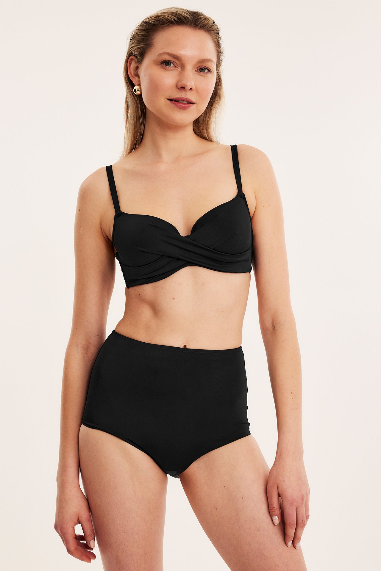 Frontvisning: kvinne i svart høy midje shaping bikinitruse, svart vridd bikinitopp og gulløreringer.