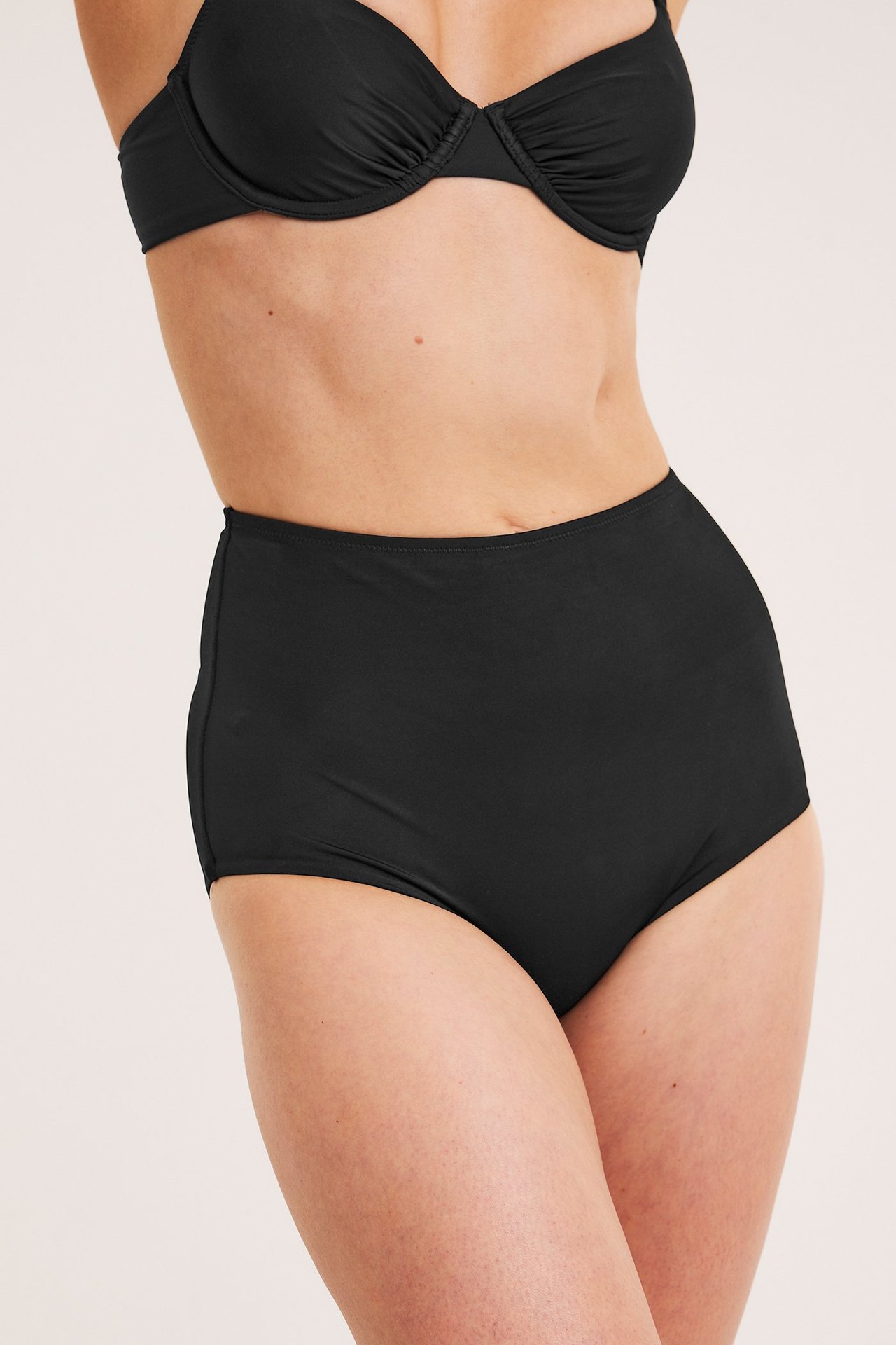 Edestä, nainen mustissa korkeavyötäröisissä muotoilevissa bikinialaosissa ja mustassa bikinitopissa.