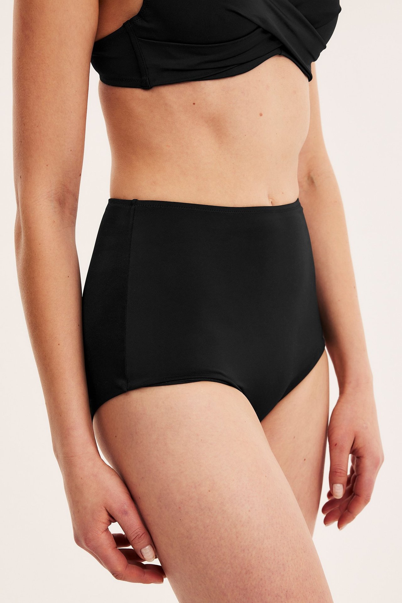 Widok z przodu kobiety w czarnych, wysokich figach bikini modelujących i czarnym skręconym biustonoszu bikini.