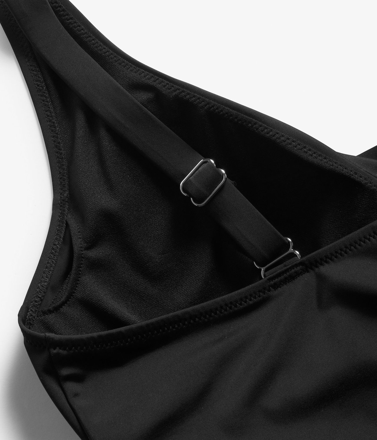 Zbliżenie czarnego kostiumu kąpielowego, ukazujące regulowany pasek ze srebrnymi metalowymi regulatorami.