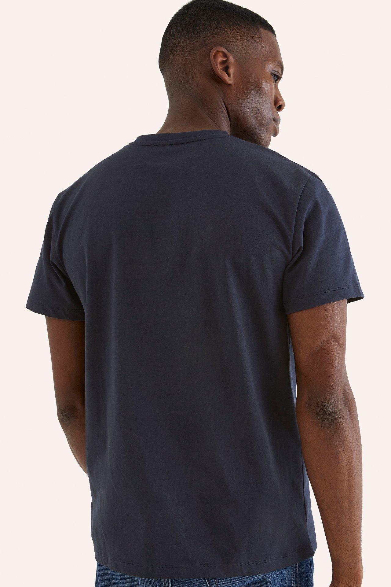 Bakfra, en mann i en mørkeblå ensfarget kortermet t-skjorte og blå jeans.