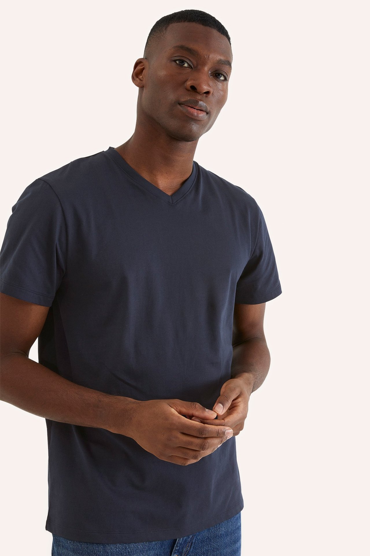 Framifrån, en man bär en mörkblå enfärgad V-ringad t-shirt i bomull och blå jeans.