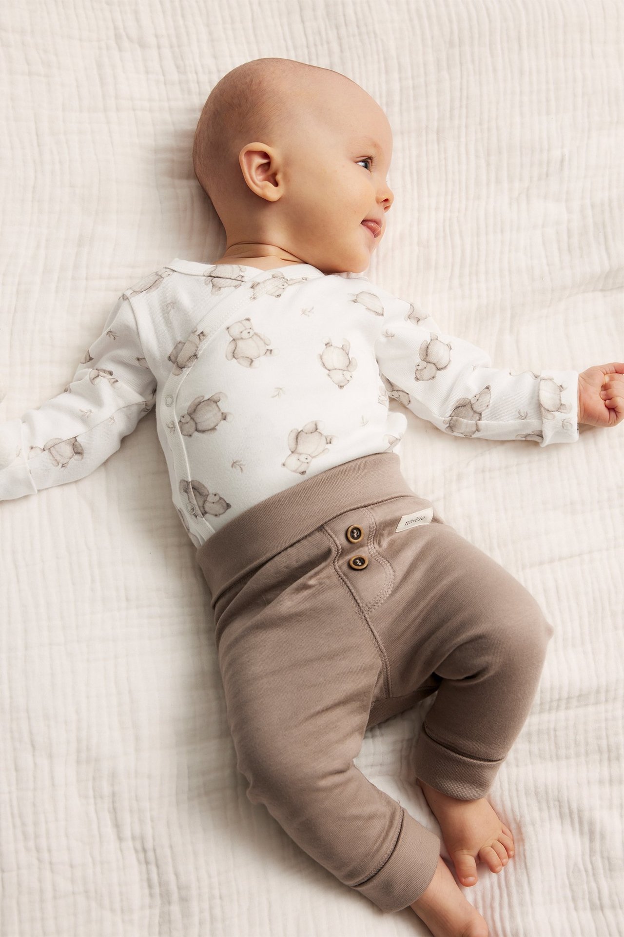 Uppifrån: baby i offwhite omlottbody med djurmönster och bruna byxor.
