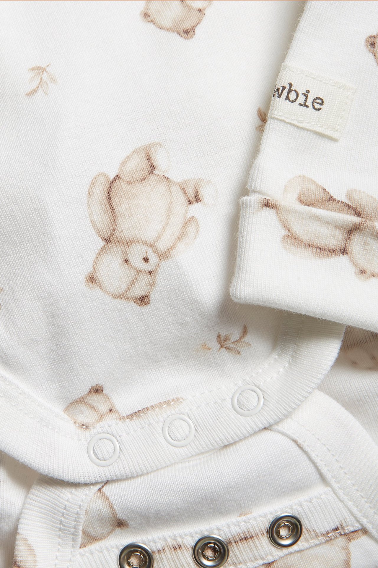 Zbliżenie na ecru bawełniane body niemowlęce z brązowym wzorem misia i zatrzaskami.