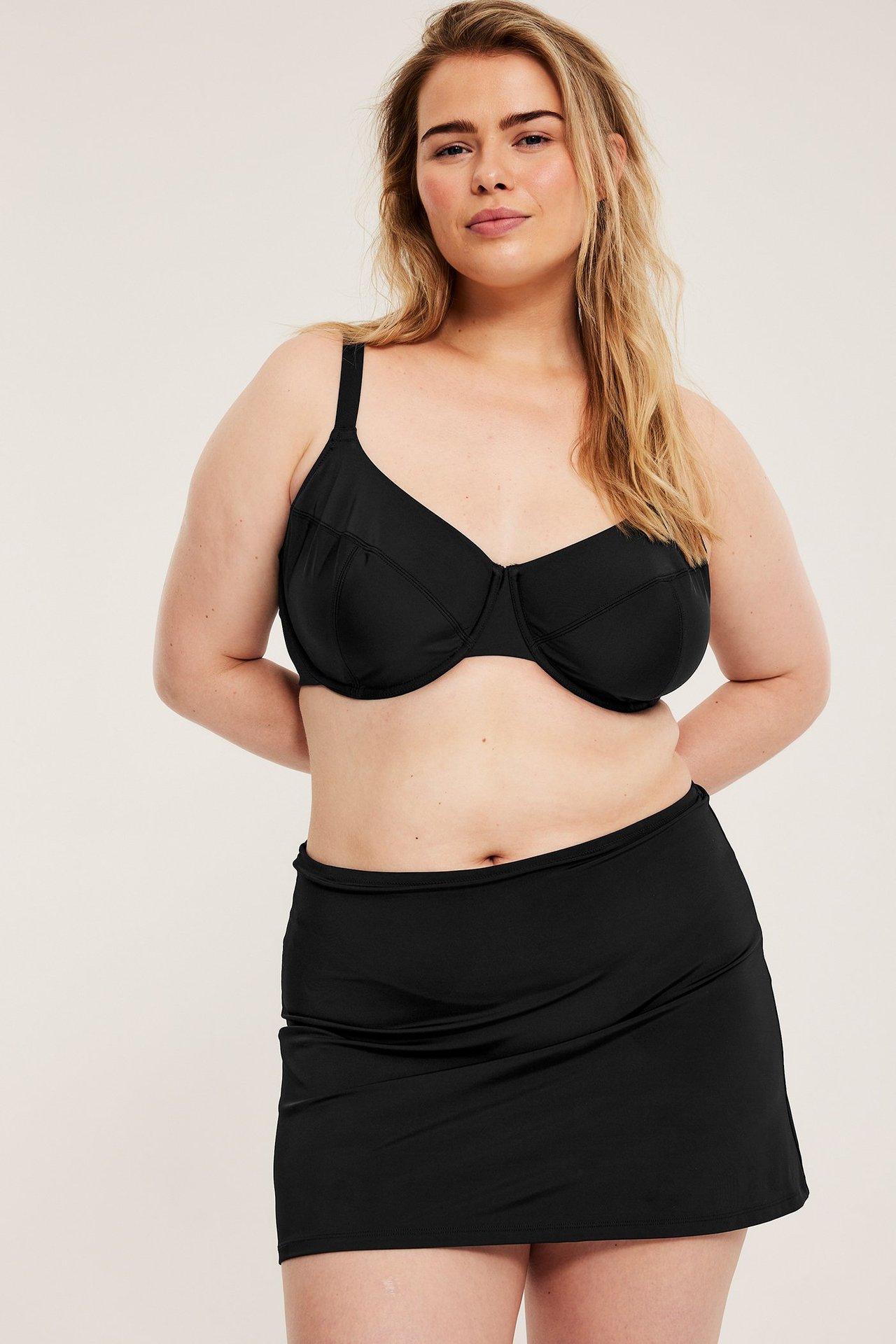 Forfra, kvinne i svart badeskjørt og matchende svart bikinitopp.