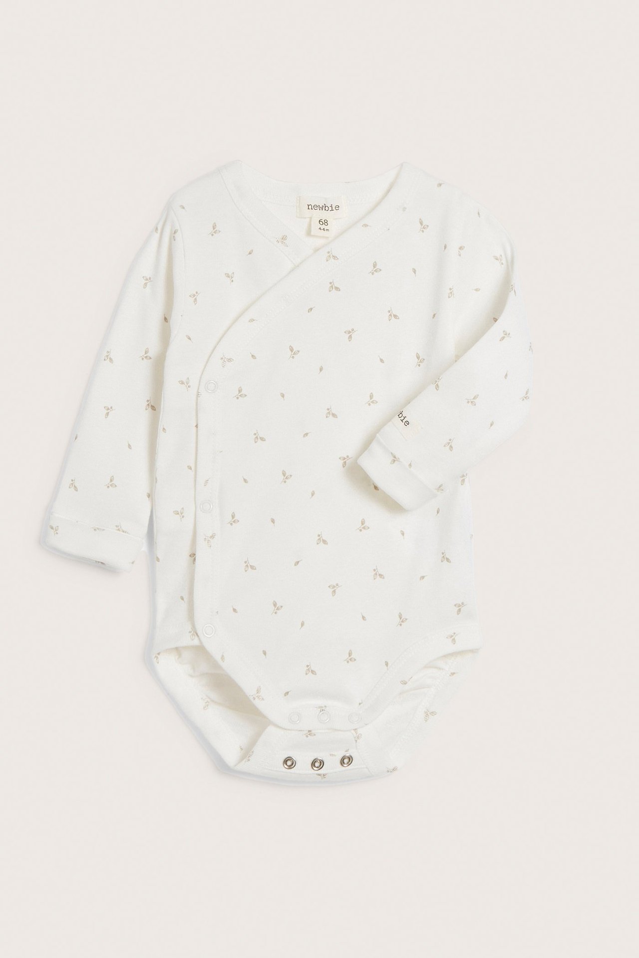 Frontvy av en beige ribbad omlottbody för baby med smått bladmönster och tryckknappar.