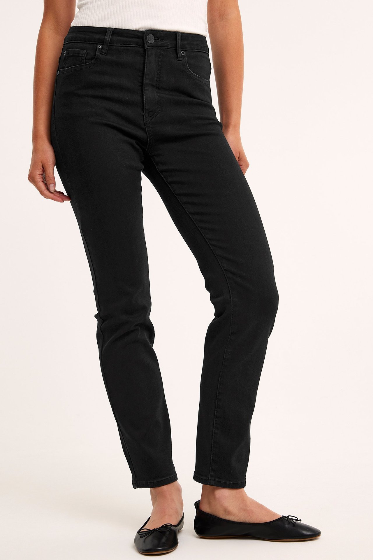 Sned framifrån: kvinna i svarta raka jeans med hög midja, vit ribbad topp och svarta ballerinaskor.