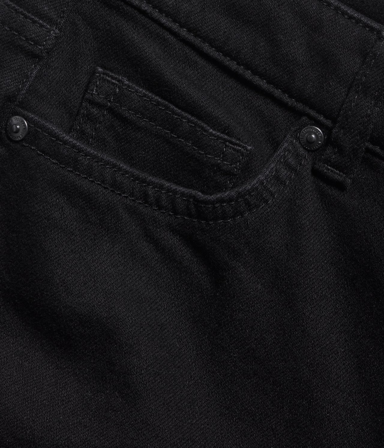 Närbild av svarta denim flare jeans, visar framfickan med en liten myntficka och metallnit.
