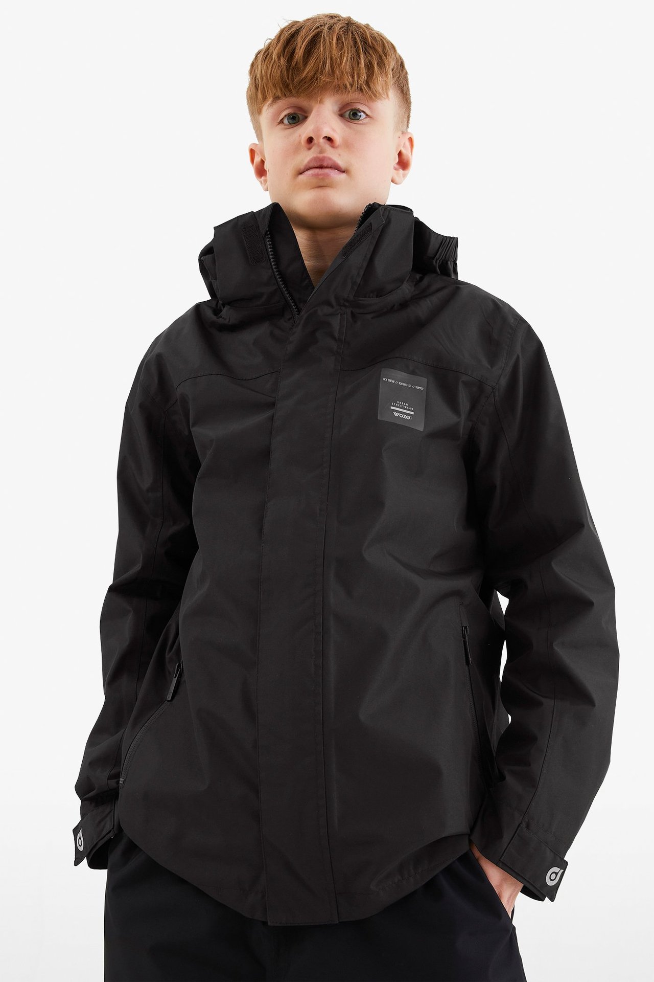 Widok z przodu dziecka w czarnej wodoodpornej kurtce softshellowej z kapturem i czarnych spodniach.