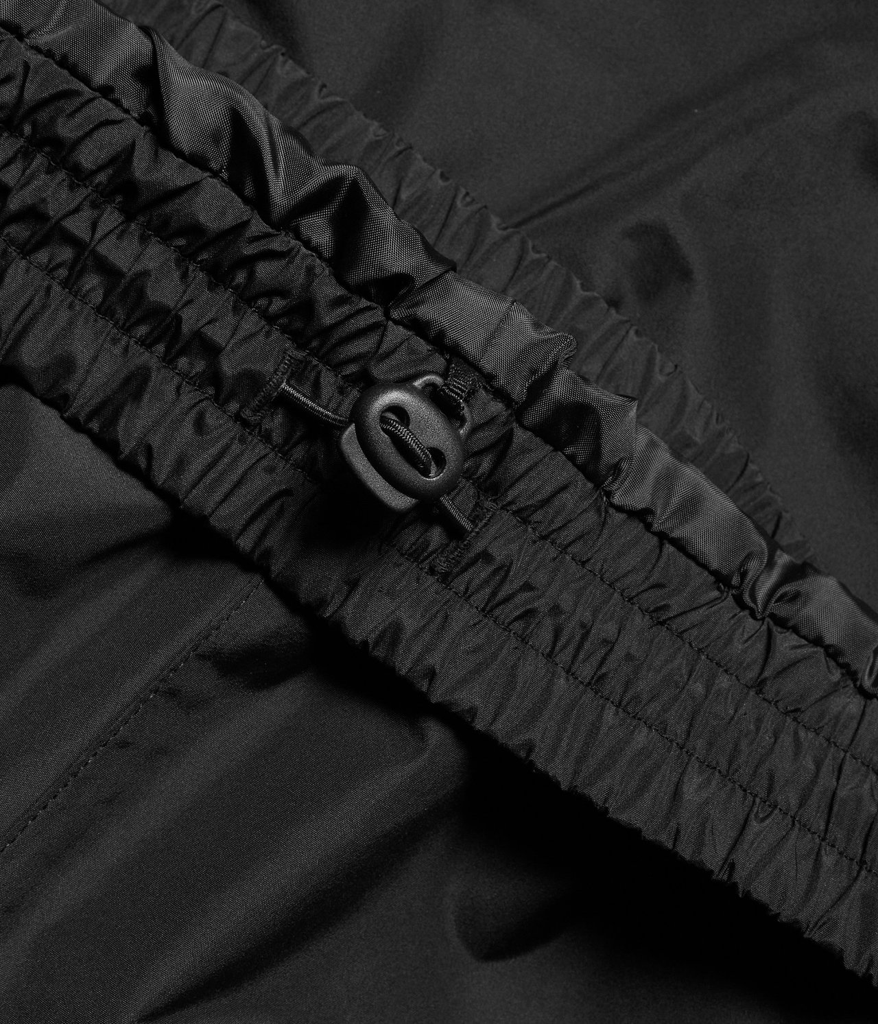 Lähikuva mustista vedenpitävistä kuorihousuista, joissa näkyy joustava vyötärö ja kiristysnyöri.