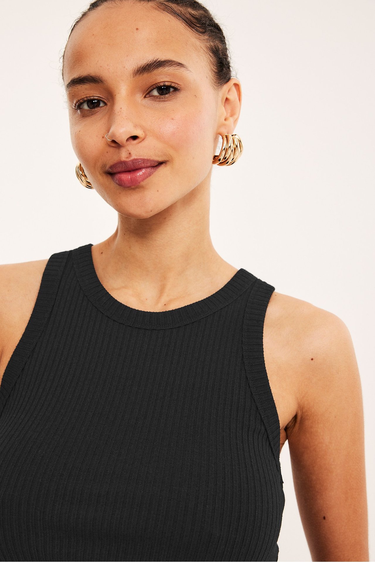 Nærbilde forfra av en kvinne i en svart ribbet singlet og gullfargede ringøreringer.