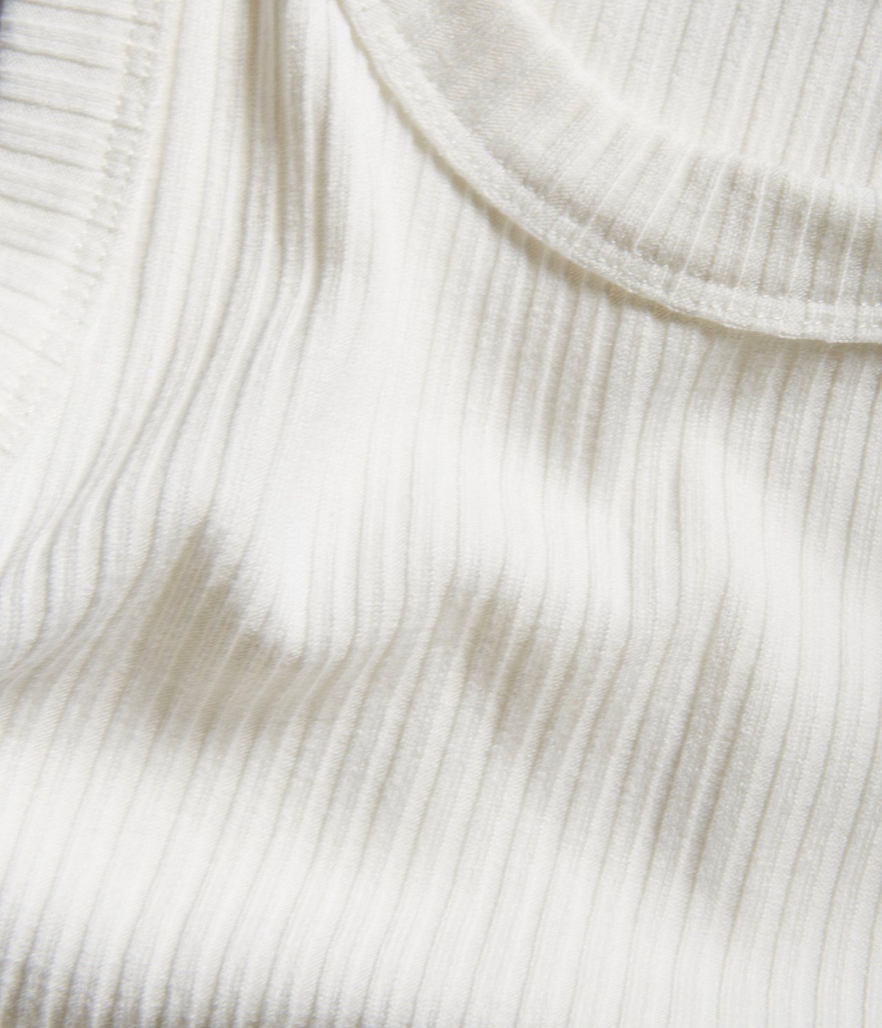 Zbliżenie na kremowy, prążkowany top, ukazujące teksturowany materiał i dekolt.