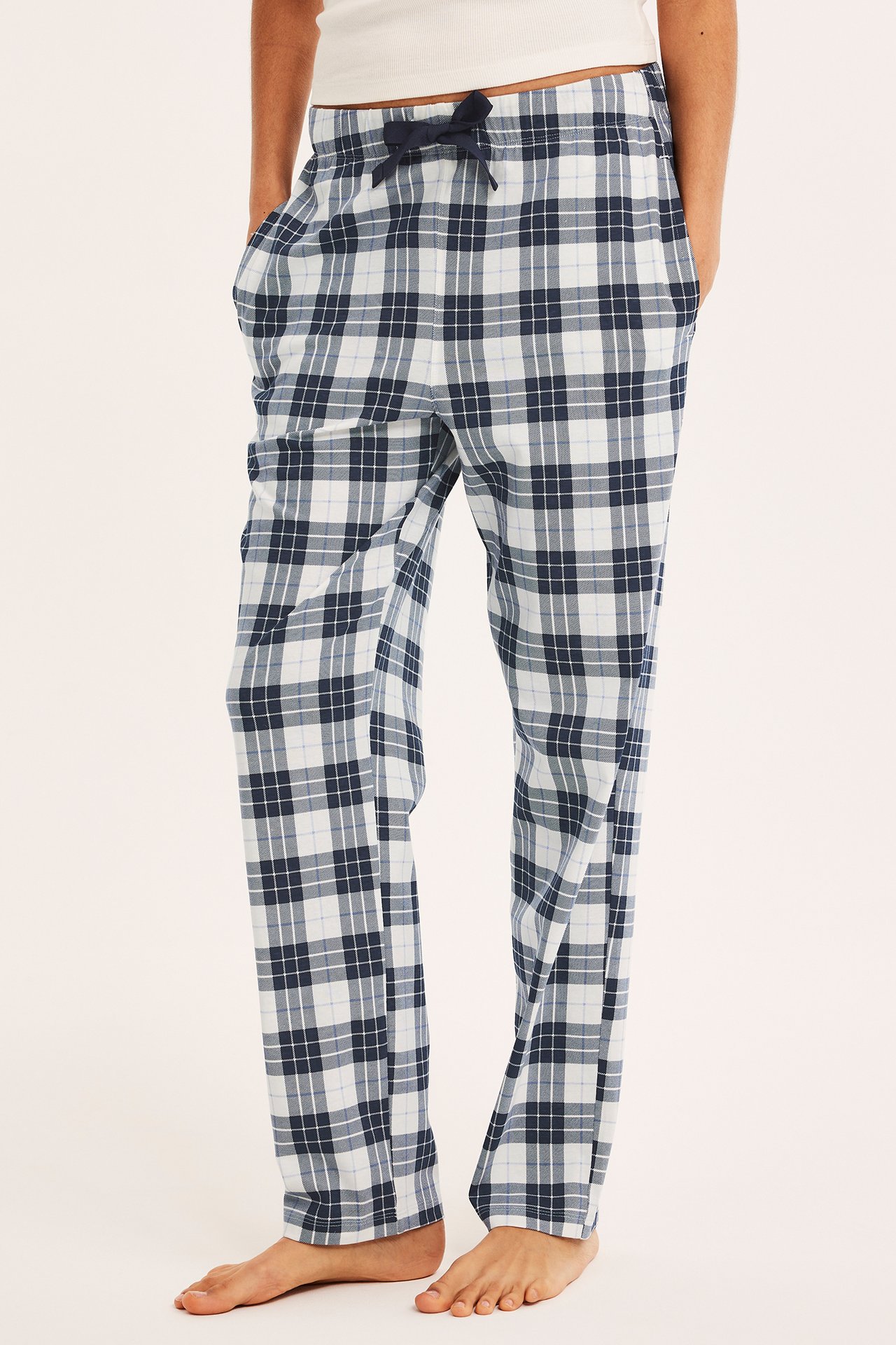 Framifrån, man i mörkblå och vitrutiga trikåpyjamasbyxor med dragsko, och ett vitt linne.