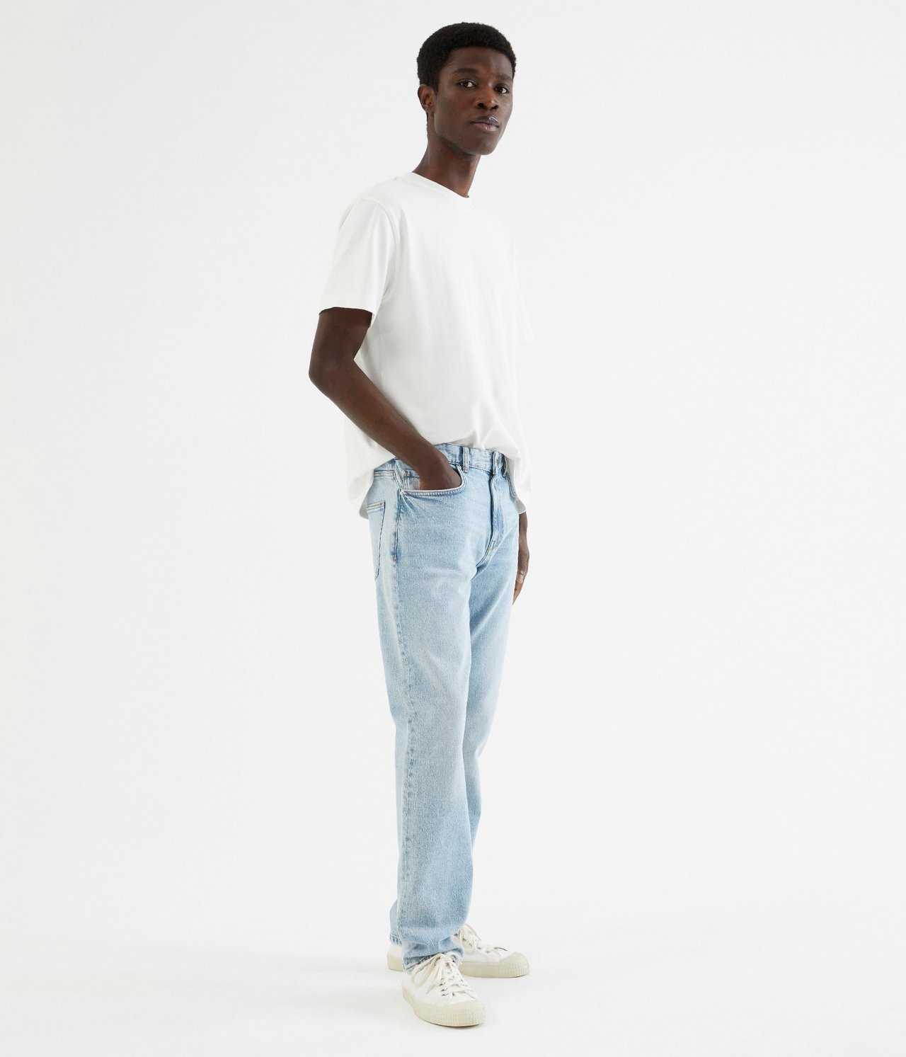 Sidebilde av en mann i lyseblå regular fit jeans, en hvit t-skjorte og lyse joggesko.