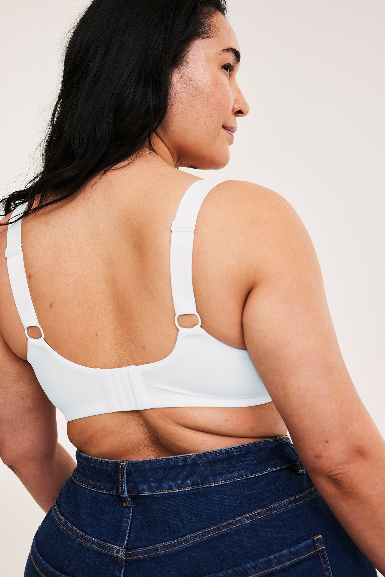 Nainen takaapäin yllään valkoinen kaarituellinen minimizer-liivit säädettävillä olkaimilla ja tummansiniset farkut.