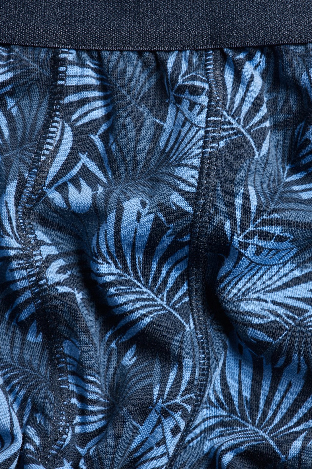 Nærbilde av blå mønstrede herrebokser med mørkeblå elastisk linning og palmbladmønster.