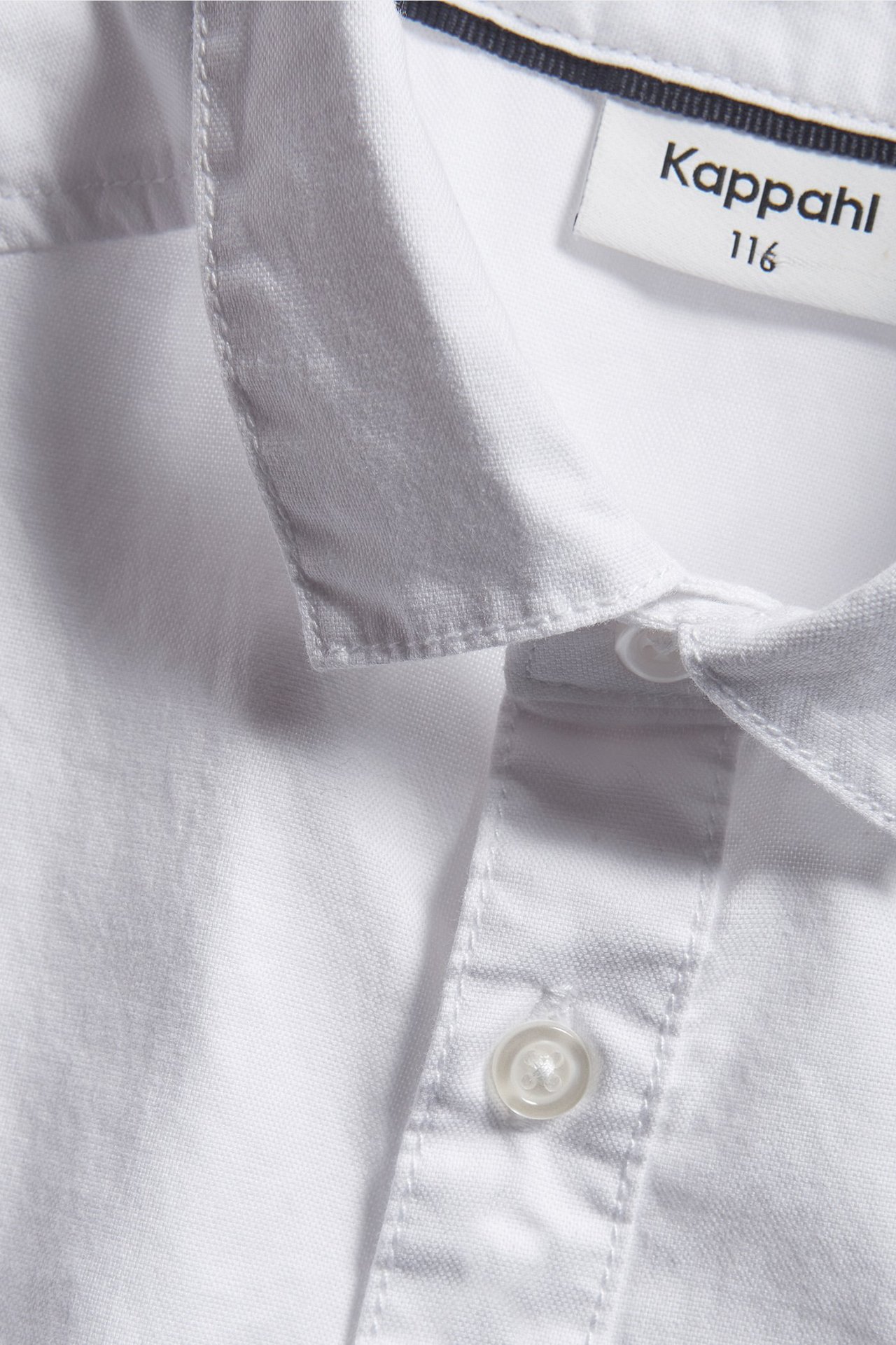 Zbliżenie na białą klasyczną koszulę oxford z bawełny dla dziecka, z kołnierzykiem i zapiętą plisą.