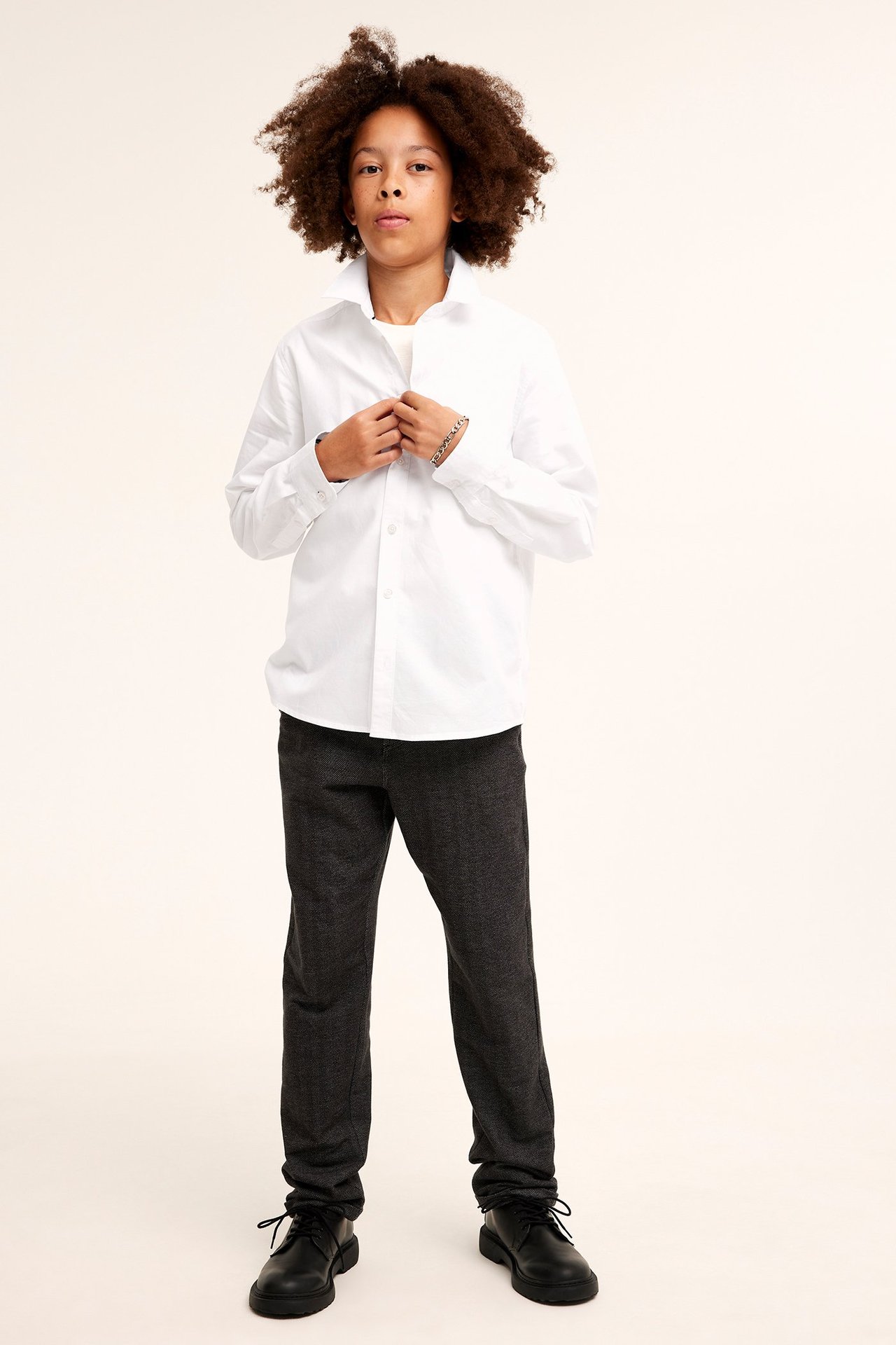 Widok z przodu dziecka w białej koszuli bawełnianej, ciemnoszarych spodniach i czarnych butach sznurowanych.