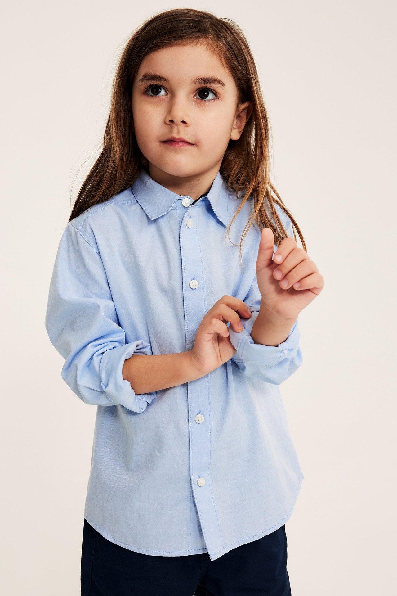 Widok z przodu: dziecko w jasnoniebieskiej bawełnianej koszuli Oxford z białymi guzikami i granatowymi spodniami.