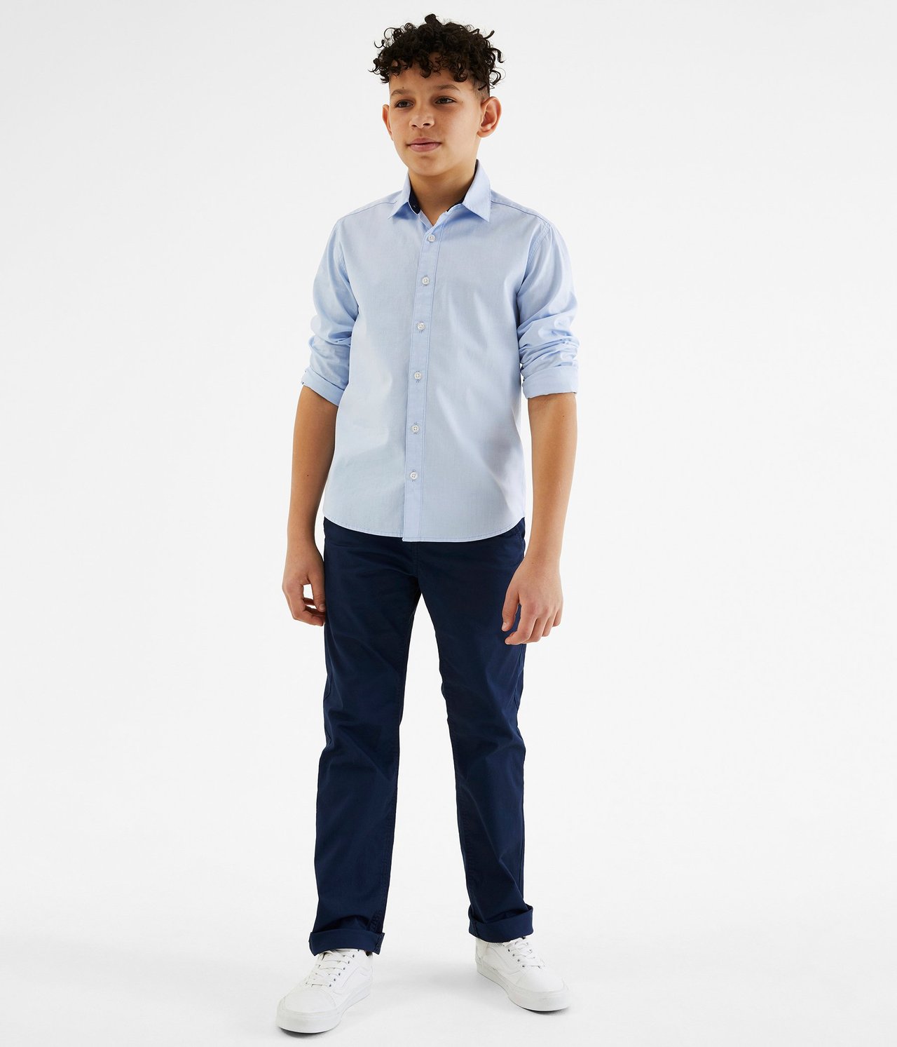 Widok z przodu: dziecko w jasnoniebieskiej koszuli oxford, granatowych spodniach i białych trampkach.