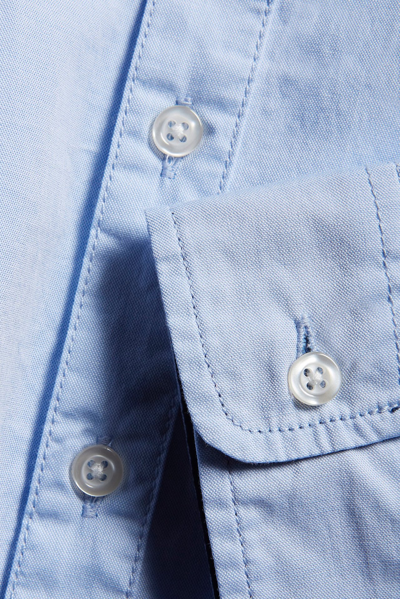 Zbliżenie jasnoniebieskiej bawełnianej koszuli oxford z białymi guzikami na plisie i mankiecie.