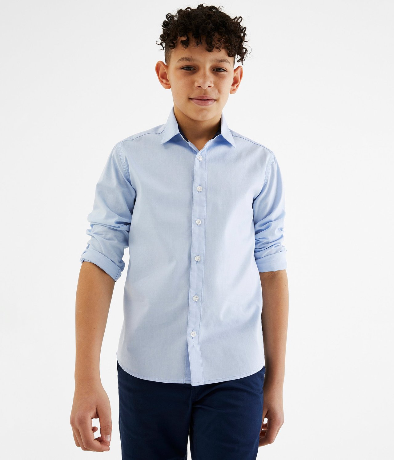 Widok z przodu: Chłopiec w jasnoniebieskiej koszuli oxford z długim rękawem i granatowych spodniach.
