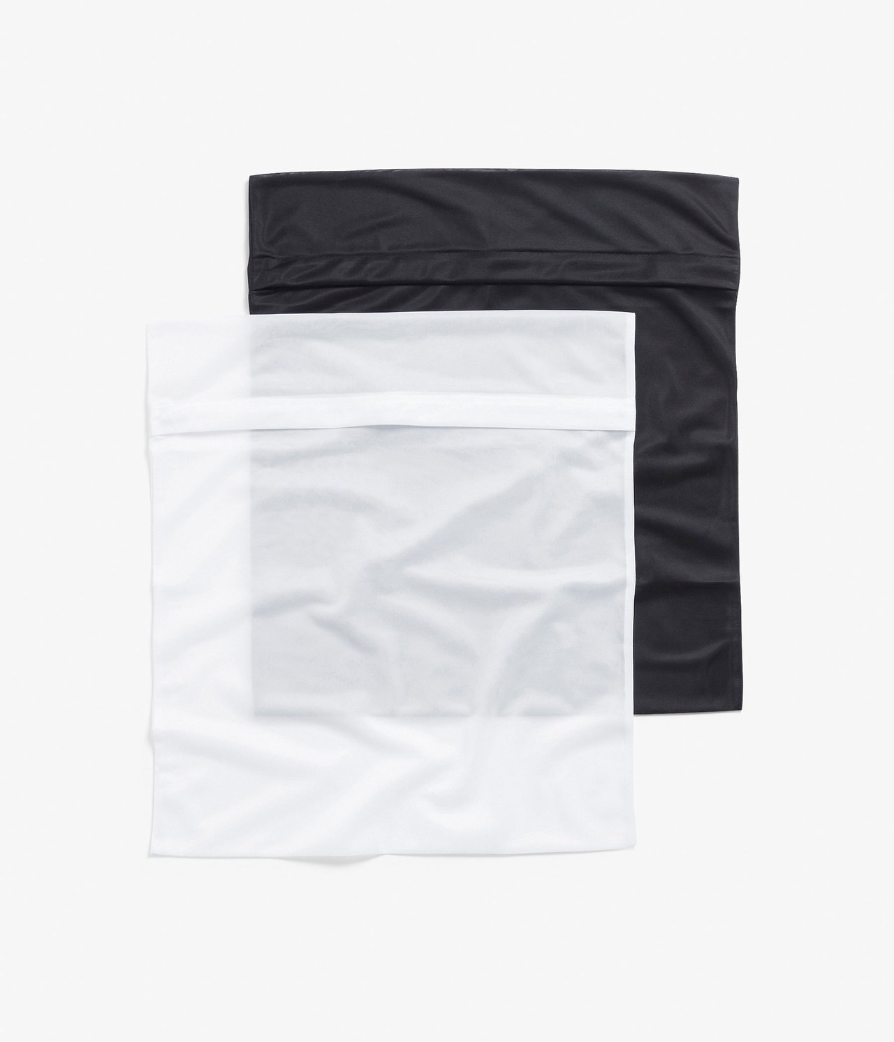 Ovanifrån, två rektangulära tvättpåsar i polyester, en vit och en svart, med dolda dragkedjor.