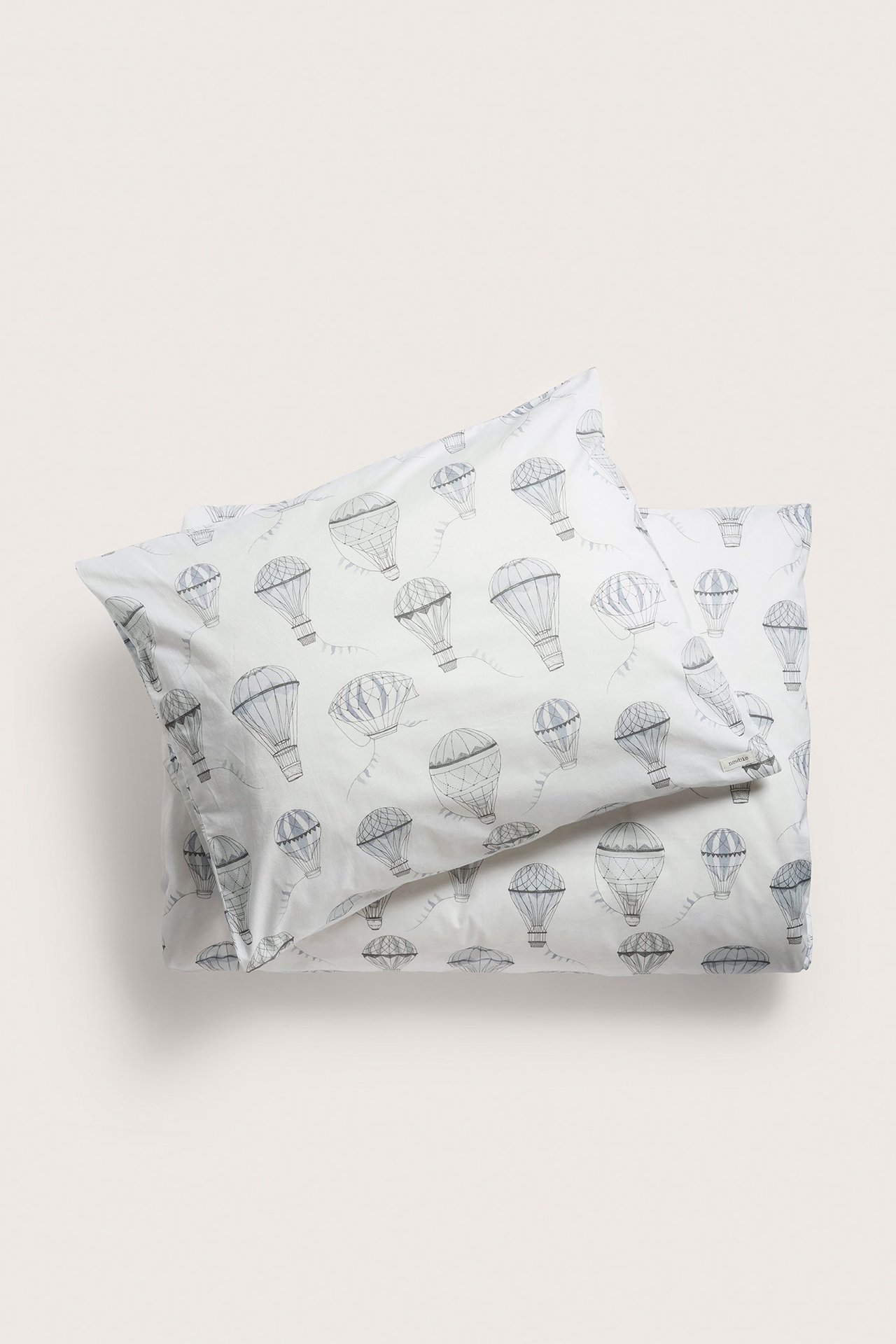 Widok z góry na komplet pościeli z bawełny w kolorze ecru z szarym wzorem balonów.