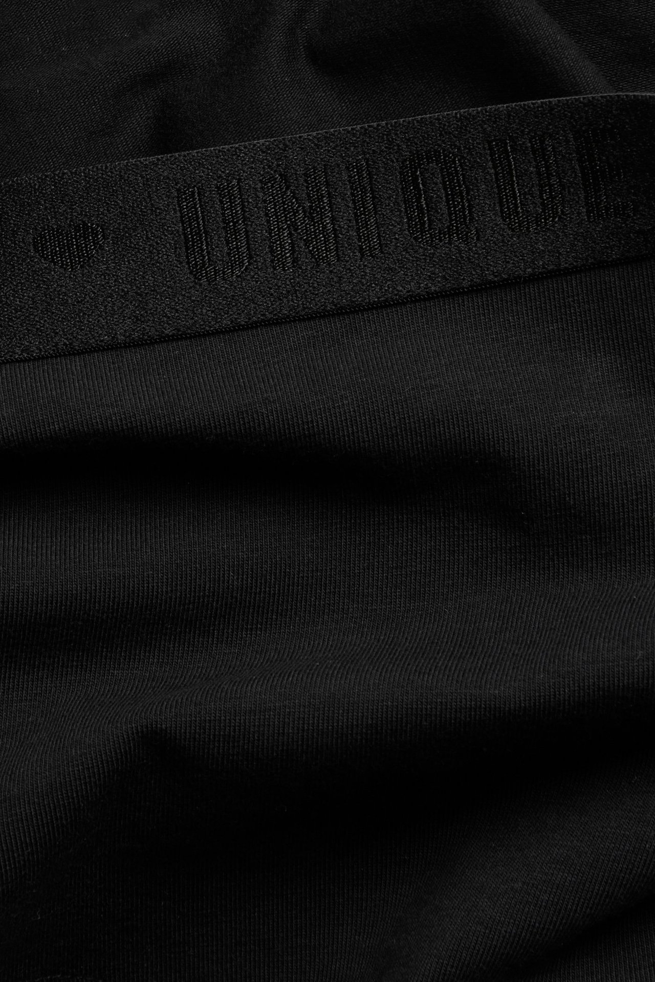 Zbliżenie na czarne bokserki z czarnym elastycznym pasem z żakardowym napisem.