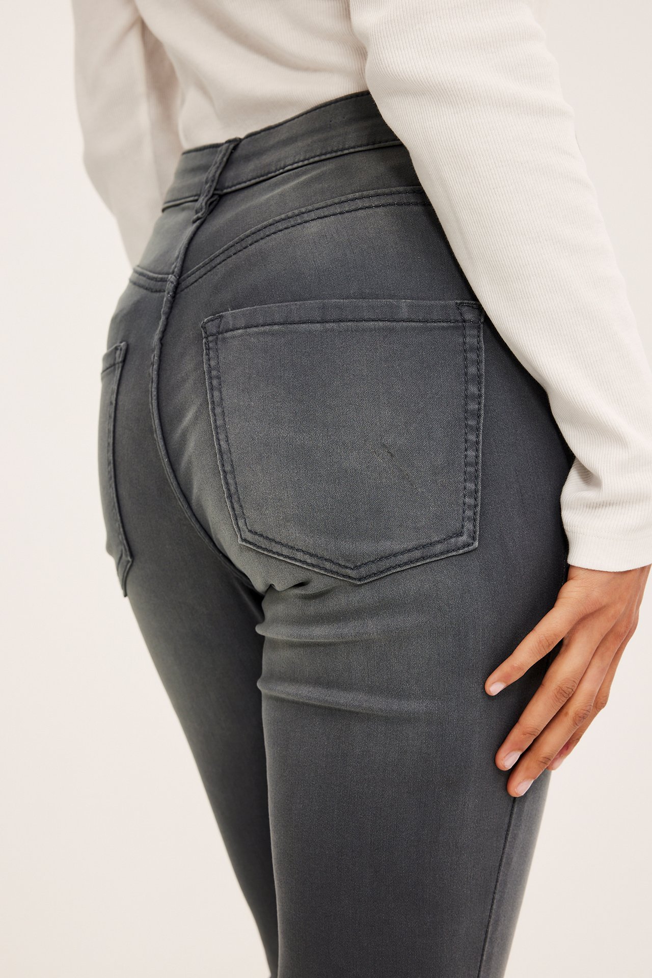 Bakifrån: kvinna i mörkgrå super slim high waist jeans och en ljus ribbad långärmad topp.