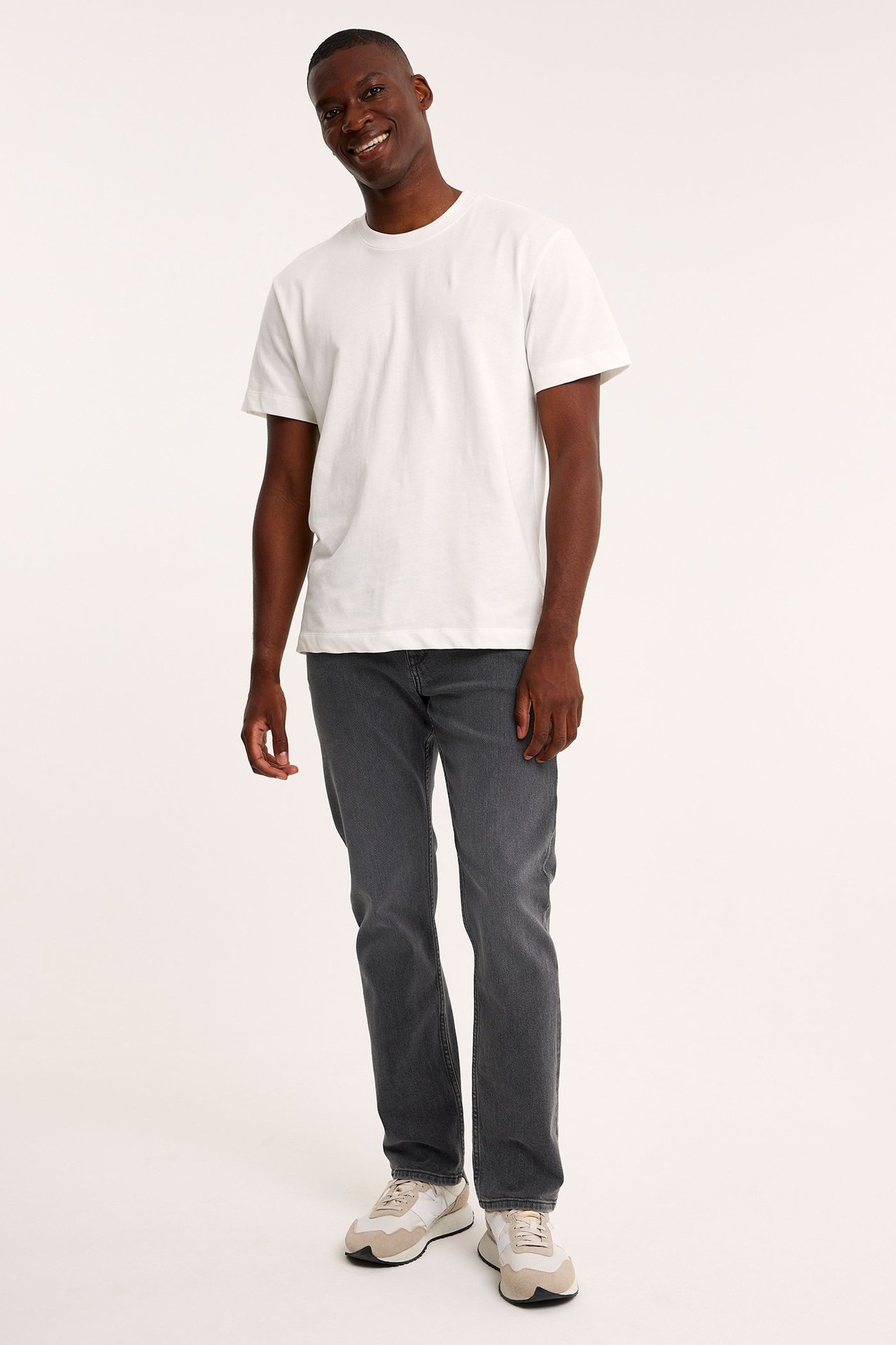 Framsida av en man i gråa regular fit denimjeans, en vit t-shirt och beige och vita sneakers.